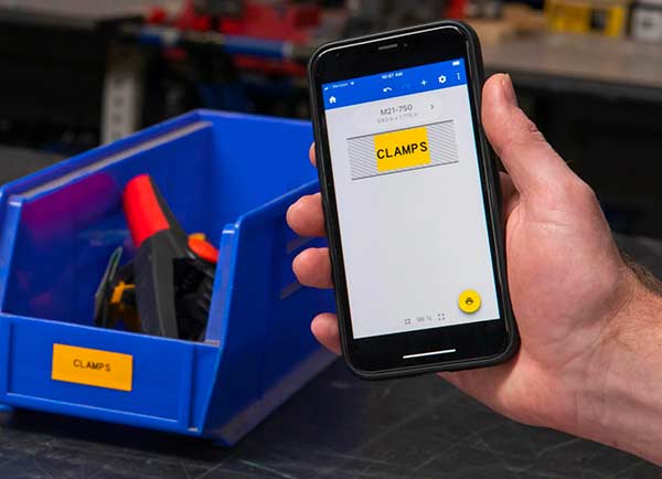 En etikettdesign på en Express Labels mobil-skärm bredvid den faktiska, utskrivna etiketten. Båda är klargula med texten ”CLAMPS” (KLÄMMOR).